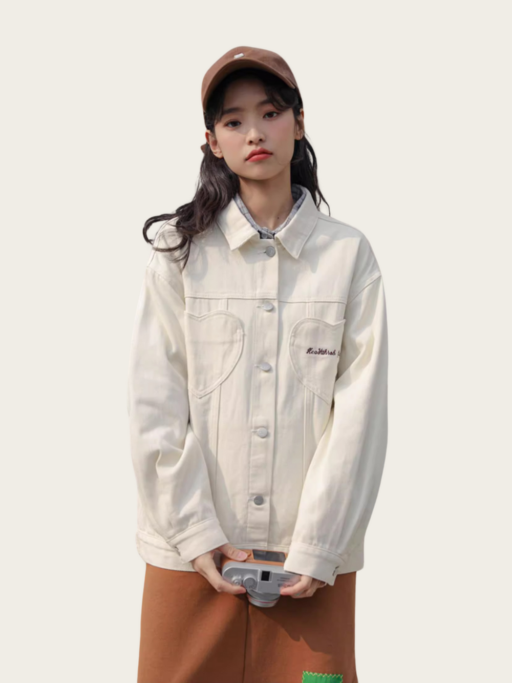 Person wearing a light-colored denim jacket and brown cap on a plain background