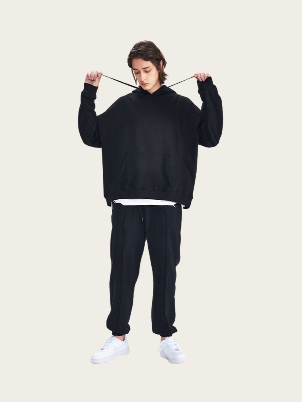 Person wearing a black hoodie and pants on a beige background