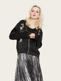Woman wearing a black bomber jacket with floral embroidery and a silver pleated skirt on a white background