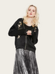 Woman wearing a black bomber jacket with floral embroidery and a silver pleated skirt on a white background