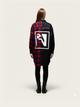 Person wearing a black and red plaid coat with a logo on the back against a white background