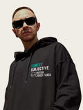 Person wearing a black hoodie with text and sunglasses on a plain background