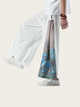 Person wearing white pants with a floral pattern and white sneakers on a light background