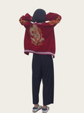 Person wearing a red embroidered jacket and dark pants on a beige background