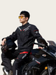Person wearing a black motorcycle suit sitting on a black motorcycle with a neutral background