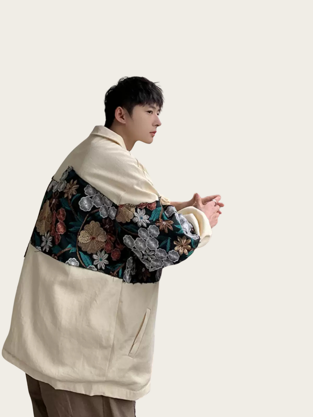 Person wearing a floral patterned jacket over a beige coat on a plain background