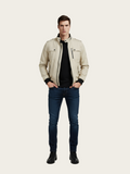 Man wearing a beige jacket, black shirt, and blue jeans on a white background