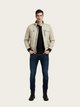 Man wearing a beige jacket, black shirt, and blue jeans on a white background