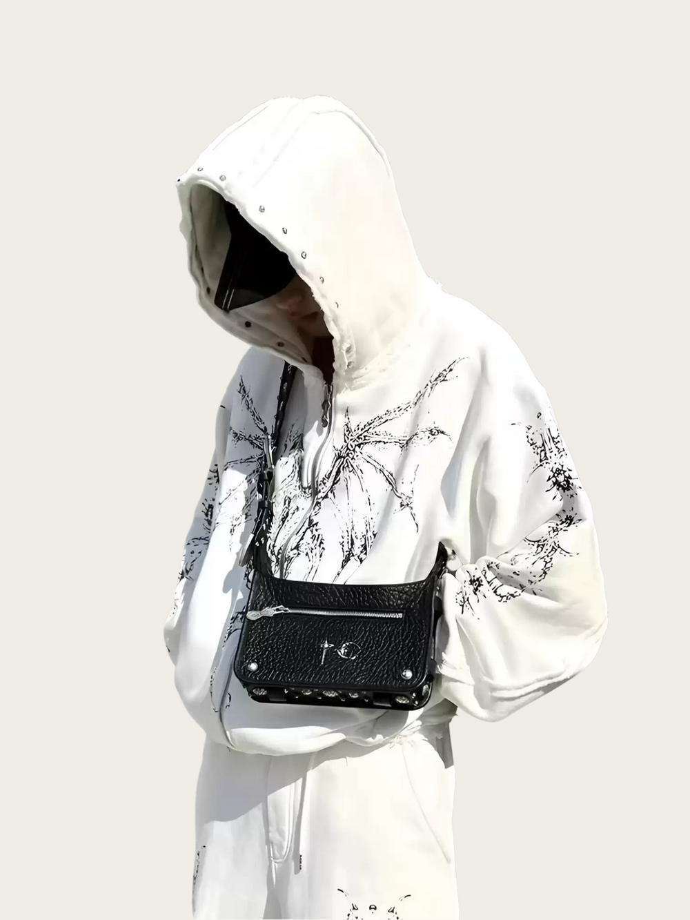 Person wearing a white hoodie with black floral patterns, holding a black handbag with a brand logo.