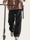 Person wearing black cargo pants and a brown jacket with a scooter on a plain background