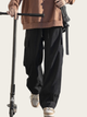 Person wearing black cargo pants and a brown jacket with a scooter on a plain background