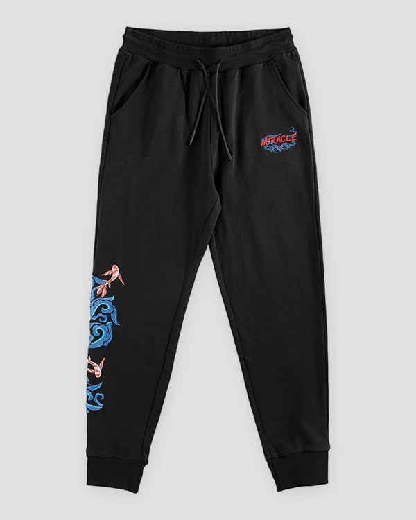 Black jogger pants laid flat with a red and blue logo on the thigh and a koi and wave on the lower leg