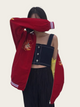Person wearing a red jacket with embroidery, over a denim top and black pants, on a beige background