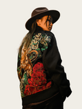 Person wearing a black jacket with colorful floral and dragon design on a plain background