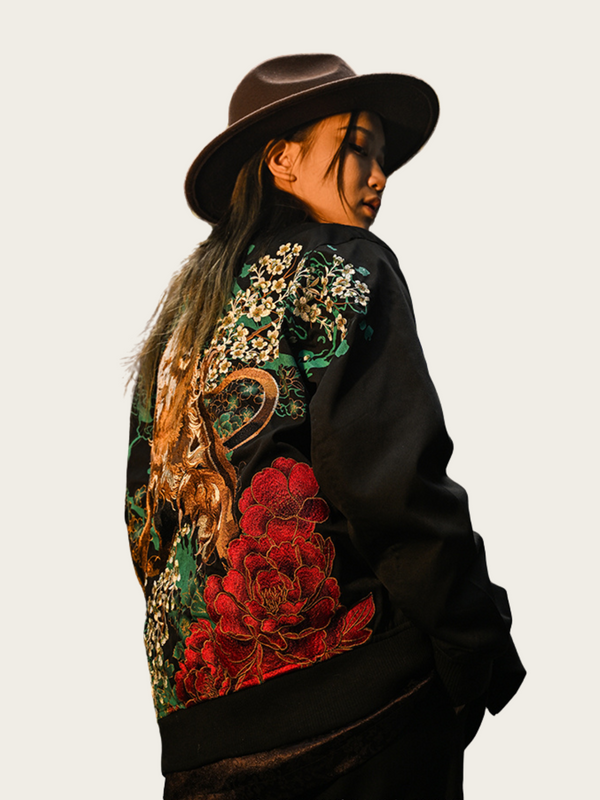 Person wearing a black jacket with colorful floral and dragon design on a plain background