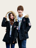 Two people wearing matching black parkas with fur hoods on a beige background