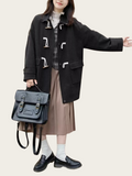 Person wearing a black coat with metal buttons, holding a black bag on a beige background