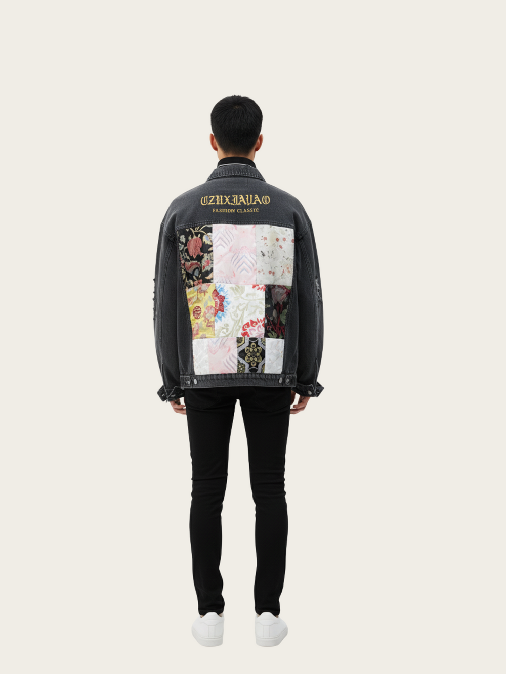 Person wearing a black denim jacket with colorful patchwork design on the back, standing against a white background.
