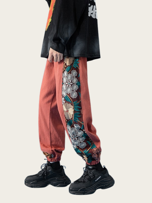 Person wearing a black jacket, red pants with floral patterns, and black shoes on a light gray background