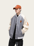 Person wearing a gray and beige varsity jacket with a red cap on a light background