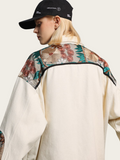 Person wearing a cream-colored jacket with floral embroidery on a light gray background