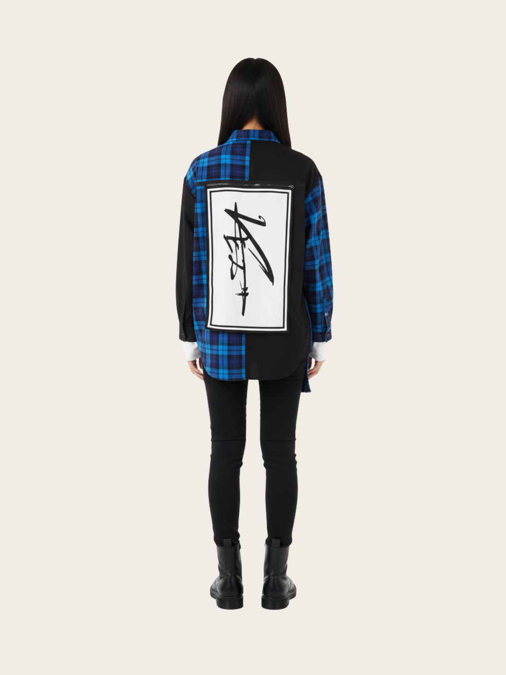 Person wearing a blue and black plaid shirt with a graphic design on the back, standing against a white background.