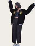 Person wearing a black varsity jacket with embroidered designs on a plain background