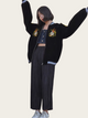 Person wearing a black varsity jacket with embroidered designs on a plain background