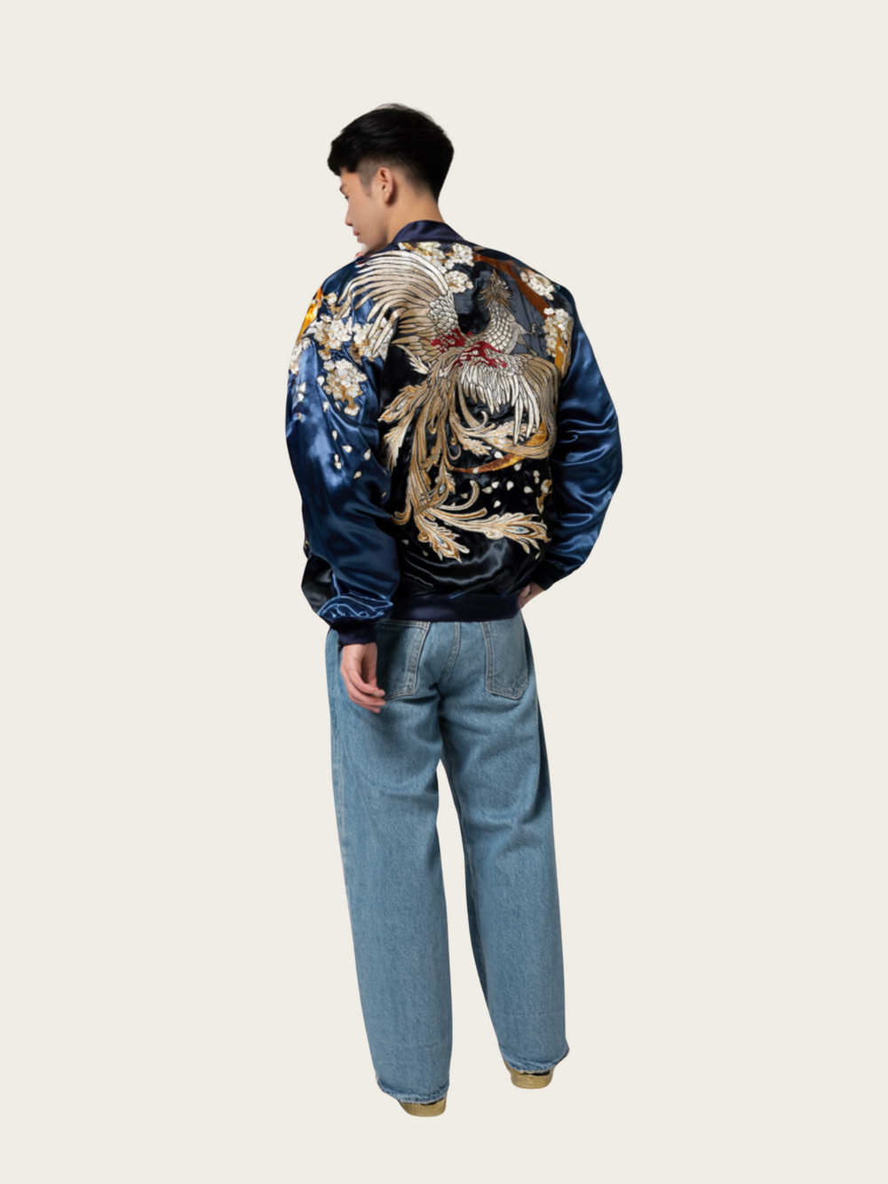 Person wearing a blue satin bomber jacket with a large embroidered design on the back, standing against a white background.