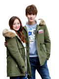 Two people wearing green parkas with fur-lined hoods on a white background