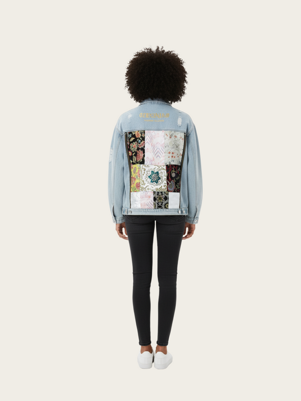 Person wearing a light blue denim jacket with a patchwork design on the back, standing against a white background.