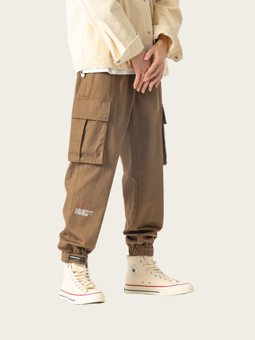 Person wearing beige cargo pants and white sneakers on a plain background