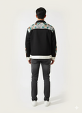 Person wearing a black jacket with floral patterns on a white background