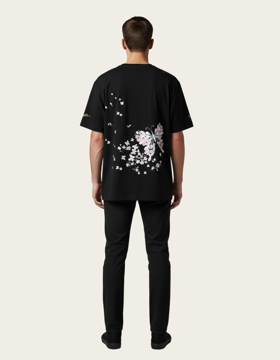 Person wearing a black t-shirt with a butterfly design on the back, standing against a gray background.