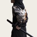 Person wearing a black hoodie with a colorful dragon design, standing against a metallic fence.