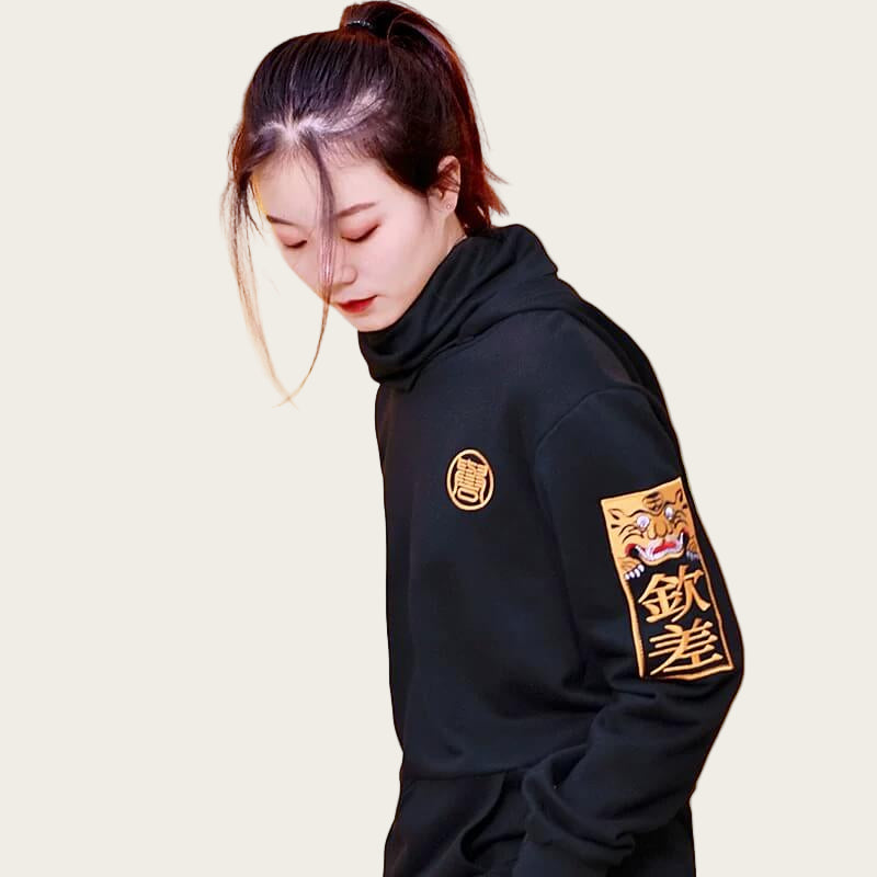 Person wearing a black hoodie with gold designs on a yellow background