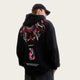 Person wearing a black hoodie with colorful designs, standing in front of red pillars.