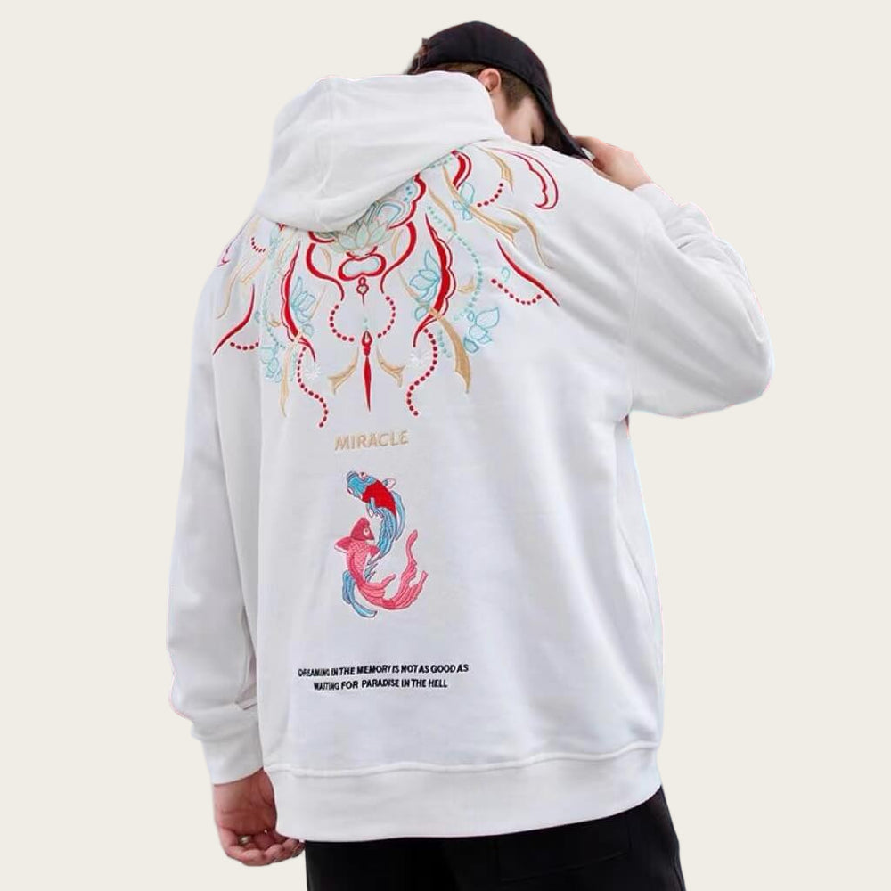 Person wearing a white hoodie with colorful designs in front of a red and white architectural background