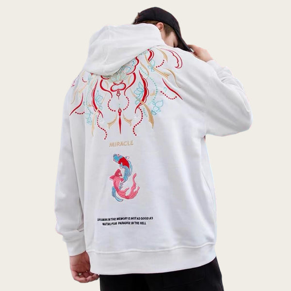 Person wearing a white hoodie with colorful designs in front of a red and white architectural background