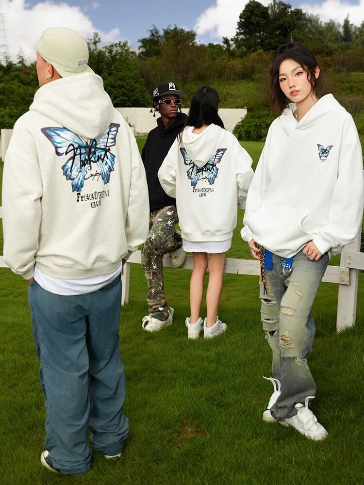 Four people wearing hoodies with a butterfly design outdoors on a grassy area.