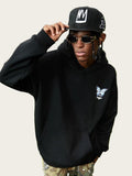 Person wearing a black hoodie with a logo, sunglasses, and a cap on a grassy field.