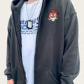 Person wearing a dark gray hoodie with a logo and a white t-shirt with text.