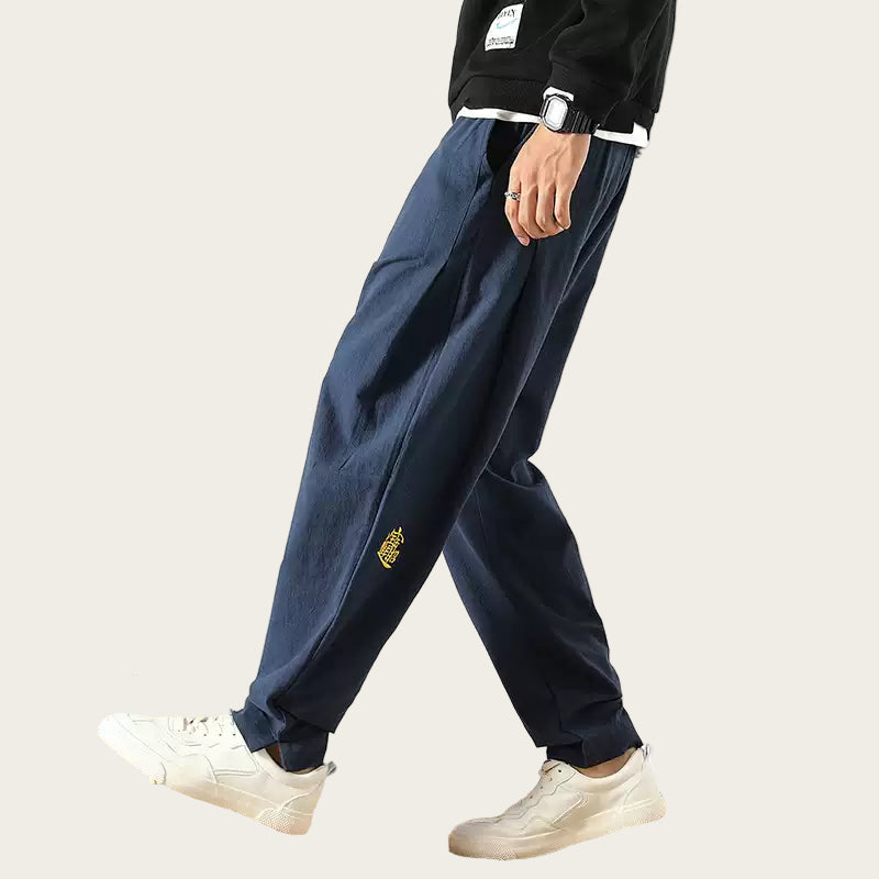 Person wearing navy blue pants with a logo, standing in a room.