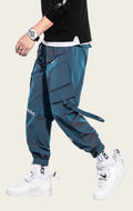 Person wearing teal cargo pants with visible branding, white sneakers, and a black top on a yellow background.