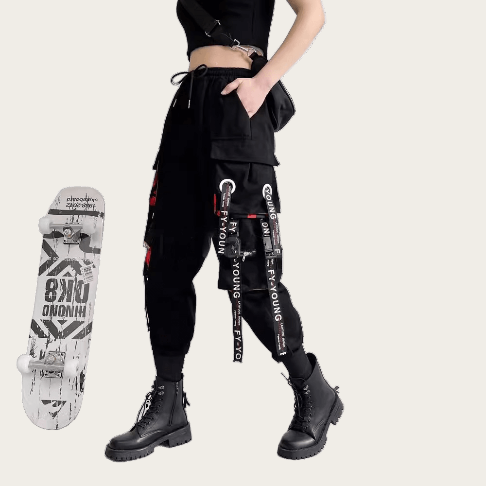 Person wearing black pants with brand logos, standing next to a skateboard on a yellow background