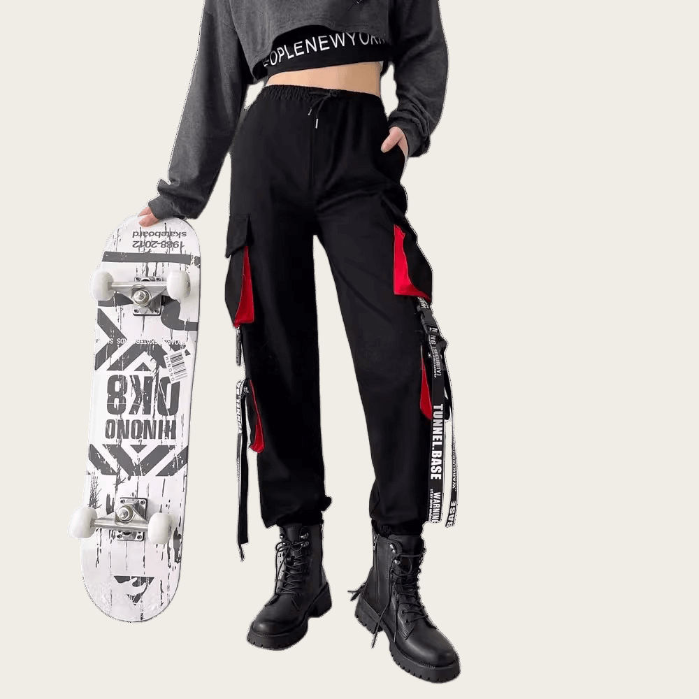 Person wearing black pants with red accents and a gray crop top, holding a skateboard.