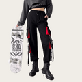 Person wearing black pants with red accents and a gray crop top, holding a skateboard.