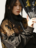 Person wearing a black and gold embroidered jacket holding a fan with East Asian characters.