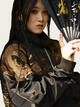 Person wearing a black and gold embroidered jacket holding a fan with East Asian characters.