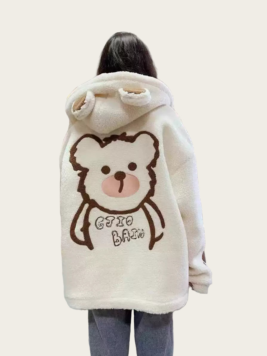 Person wearing a fluffy white hoodie with a cartoon bear design in a kitchen.
